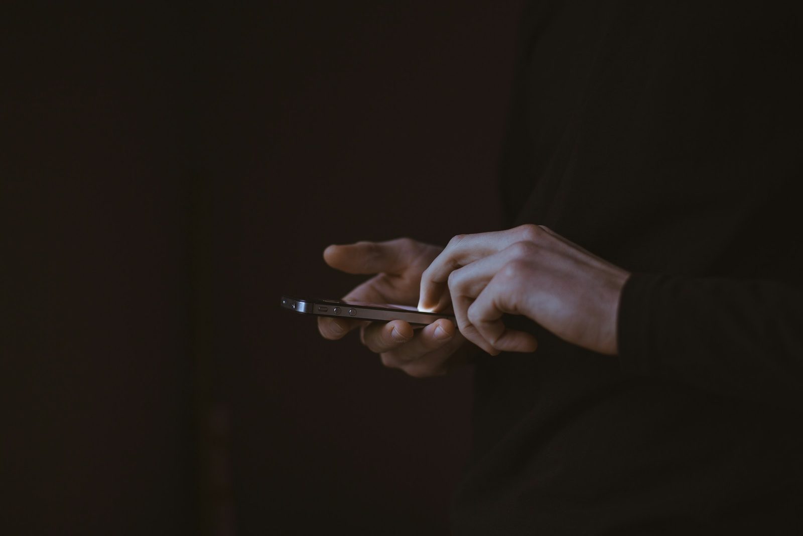 A person tapping on a phone held sideways against a dark background