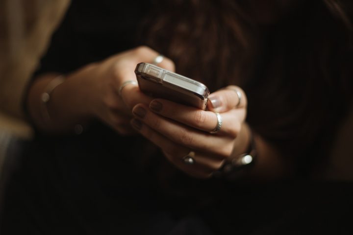 Close up of hands holding a phone and typing a message in low light